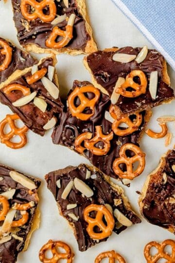 Broken pieces of cracker candy topped with chocolate, toffee, and pretzels on a baking sheet.